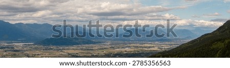 Panoramic view of a mountain valley with patchwork farmland and distant peaks near Chilliwack, British Columbia, Canada.