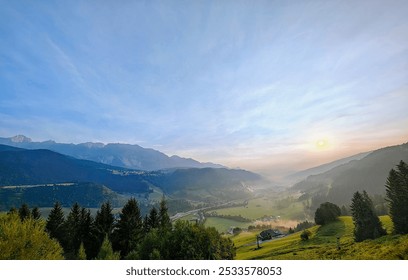 A panoramic view of a mountain valley at sunrise with a clear blue sky, lush green fields, and scattered houses - Powered by Shutterstock