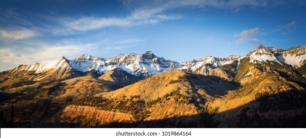 Panoramic view of a mountainside lit by a setting sun in the rocky mountains.  The glow of the sun illuminates the fall colors, along with the first snow found high up in the mountain peaks.  - Powered by Shutterstock