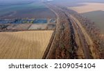 Panoramic View of Moving Freight Train Along Railway Tracks Among Trees Between Agricultural Fields on an Autumn Day. Landscape Freight Cars or Railway Wagon Rides on Railroad. Top View Rail freight