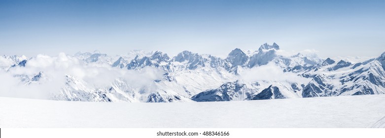 Panoramic view of a Mt. Elbrus ski slope and snowy Greater Caucasus mountains on the horizon at winter cold sunny day.