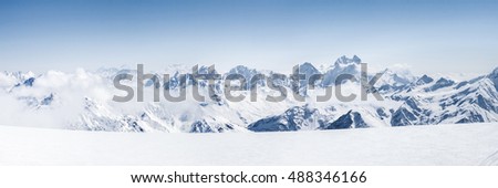 Panoramic view of a Mt. Elbrus ski slope and snowy Greater Caucasus mountains on the horizon at winter cold sunny day.