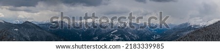 panoramic view, near 180 degrees, of a beautiful mountain environment in the afternoon at the end of winter season. mountain ranges covered in snow. dark snowy clouds dominating the landscape