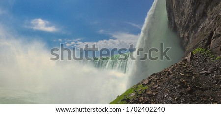 A panoramic view of Niagara falls in Canada from bellow with grey rock, massive waterfalls and blue sky