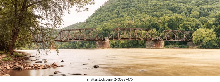 Panoramic view of old, rusty iron railway bridge spanning wide river in West Virginia state close to wild camp place for travelers and fishemans in America, Usa
