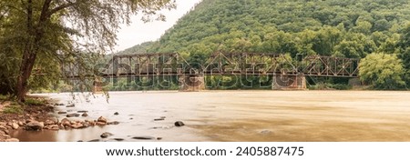 Panoramic view of old, rusty iron railway bridge spanning wide river in West Virginia state close to wild camp place for travelers and fishemans in America, Usa
