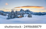 Panoramic view on Alpe di Siusi meadow with small wooden log cabin and first snow. Snowy hills with orange larch and Sassolungo and Langkofel mountains group. Seiser Alm, Dolomites, Italy.