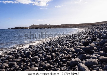 Panoramic view on black stone pebble beach Playa Colmenares near Amarilla, Golf del Sur, Tenerife, Canary Islands, Spain, Europe. Montana Amarilla in the back. Tranquil waves from the Atlantic Ocean