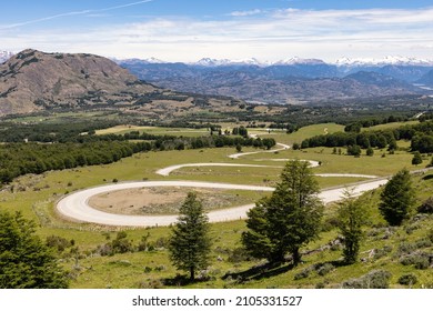 Panoramic View On A Curvy Road Going Down A Hill With Mountains In The Background