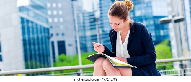panoramic view on dynamic young executive girl taking notes on her agenda, outside. Symbolizing a job search or a trade of outsourcing