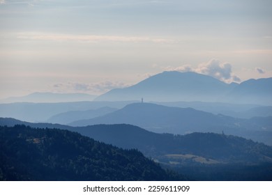 A panoramic view on endless mountain chains in Carinthia, Austrian Alps. The mountains are shrouded in fog. In the distance you can see the viewing tower Pyramidenkogel. Serenity and calmness