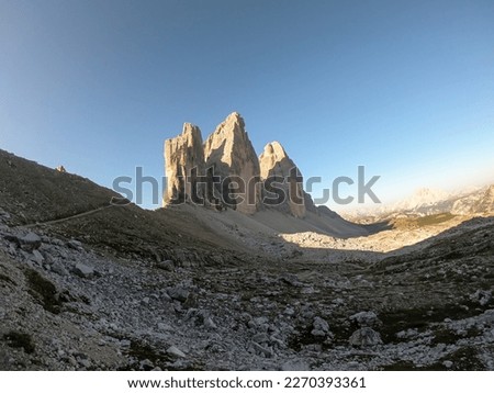 A panoramic view on the first sunbeams reaching the top of the Tre Cime di Lavaredo (Drei Zinnen), Italian Dolomites. The peaks shine with pink and orange. New day beginning in the high mountains