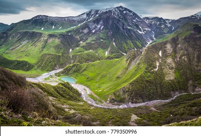 Panoramic view on the Kazbek mountains and the green valley crossed with roads and with a blue lake in Georgia
