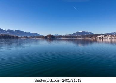 Panoramic view on lake Faakersee in Austrian Alps, Carinthia, Austria. Lake is surrounded by high snow capped mountains. Calm water surface with reflections of landscape. Looking at Dobratsch peak - Powered by Shutterstock