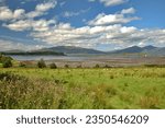 Panoramic view on the Loch Linnhe in low tide, green meadow with flowers, white lighthouse visible in the distance,  mountains at the background, Port Appin on west coast of Scotland y 