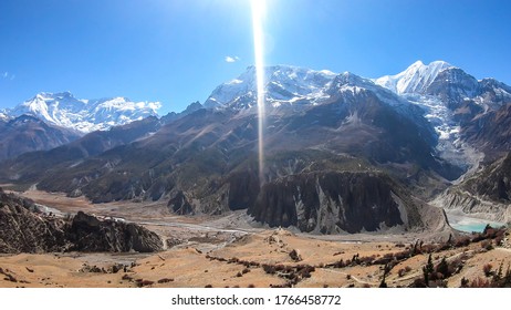 A panoramic view on Manang valley from Praken Gompa, Nepal. High Himalayan ranges around. There is a small lake in the valley. Snow capped peaks of Annapurna Chain. Harsh landscape.