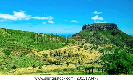 Panoramic view on massive volcanic plug Fortaleza de Chipude overlooking western coast of La Gomera, Canary Islands, Spain, Europe. Village in valley embedded lush green hills. Road to Valle Gran Rey
