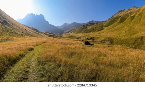 A panoramic view on the sharp mountain peaks of the Chaukhi massif in the Greater Caucasus Mountain Range in Georgia, Kazbegi Region. A hiking trail on a green alpine pasture. Georgian Dolomites.