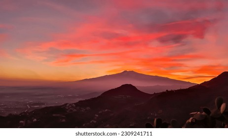 Panoramic view on silhouette of hills during twilight. Watching beautiful sunset behind volcano Mount Etna near Castelmola, Taormina, Sicily, Italy, Europe, EU. Clouds with vibrant red orange colors - Powered by Shutterstock