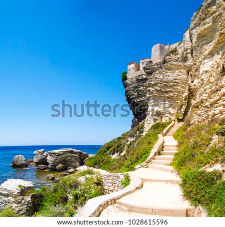 Panoramic view on the stairs going up to the mountain fortress with the rocky clear water sea shore. Bonifacio, Corsica, France.