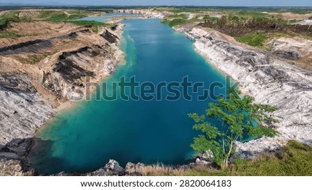 Panoramic view of an open-pit coal mine featuring exposed coal-bearing strata surrounding a striking turquoise mining void. The crystal-clear pit lake contrasts with the layered sedimentary rocks and excavated landscape, creating a remarkable geological scene that illustrates coal geology, stratigraphy, mining engineering, mineral resources, and post-mining landscape transformation.