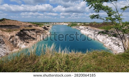 Panoramic view of an open-pit coal mine featuring exposed coal-bearing strata surrounding a striking turquoise mining void. The crystal-clear pit lake contrasts with the layered sedimentary rocks and excavated landscape, creating a remarkable geological scene that illustrates coal geology, stratigraphy, mining engineering, mineral resources, and post-mining landscape transformation.