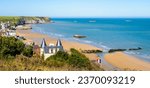 Panoramic view over Arromanches beach and Cap Manvieux in Normandy, France, on a sunny day, with remains of the WWII artificial Mulberry harbor lying on the sand and in the sea.