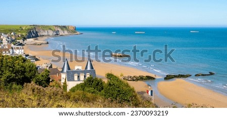 Panoramic view over Arromanches beach and Cap Manvieux in Normandy, France, on a sunny day, with remains of the WWII artificial Mulberry harbor lying on the sand and in the sea.