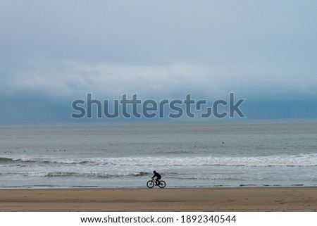 Panoramic view over the beach of Texel island, the Netherlands with a lone biker on his bicycle riding along the shoreline with dark storm clouds on the horizon