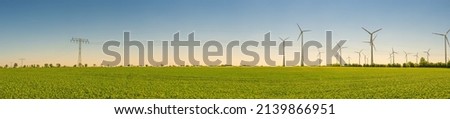 Panoramic view over farm landscape with agricultural field, wind turbines to produce green energy and high voltage power lines in Germany, at Spring and blue sunset sky