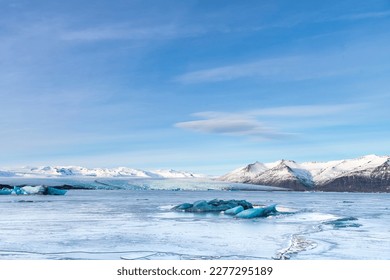 Panoramic view over the frozen glacial lagoon with the terminus or end of the Jokulsarlon glacier, Iceland with in forefront various blue arctic icebergs and snow covered mountain range in background