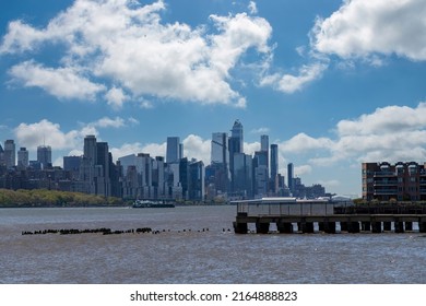 Panoramic View Over The Hudson River From The New Jersey Shore In Southerly Direction Towards Lower Manhattan New York City, USA With Skyline Of Skyscrapers Against A White Clouded Blue Sky