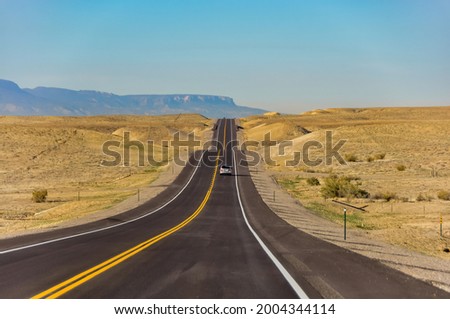 Panoramic view over the length of US Route 160 in the southwestern corner of Colorado, USA in rolling desert landscape with mountain range in back and single car on road