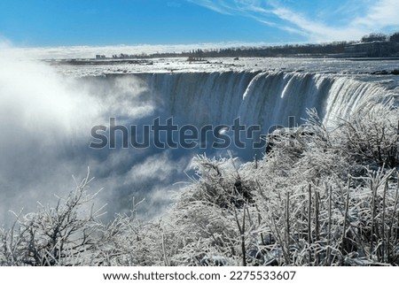 Panoramic view over the Niagara Falls, ON, Canada during winter with water spray from the falls creating layers of white ice on the bushes and vegetation in forefront