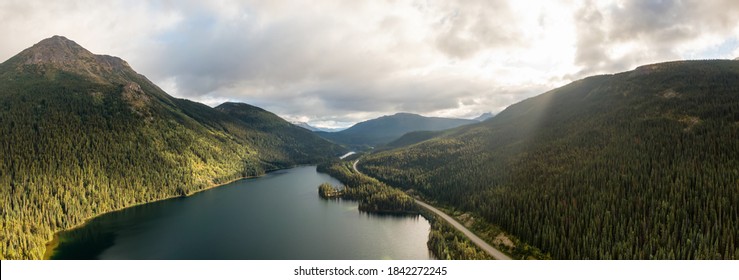 Panoramic View of Peaceful Lake alongside Scenic Road, surrounded by Mountains in Canadian Nature. Aerial Drone Shot. Taken near Stewart-Cassiar Highway, Northern British Columbia, Canada.