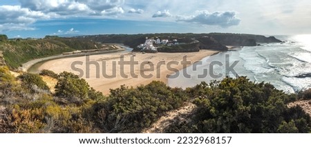 Panoramic view of Praia de Odeceixe Mar Surfer beach with golden sand, atlantic ocean waves, river bend and white houses of Odeceixe village. Rota Vicentina coast, Odemira, Portugal.