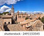 Panoramic view of Pueblo Español Open-air Museum with traditional Spanish buildings, terracotta roofs, a bell tower, and urban cityscape under a blue sky with clouds