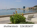 A panoramic view of The Riva Waterfront in Split, Croatia with a colorful flowers, a bench and sailboats in the marina.