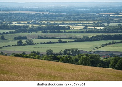 A panoramic view of rolling green fields and farmland with wind turbines in the distance