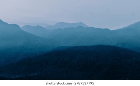 Panoramic view of rolling mountain ranges covered in dense forest during misty blue hour twilight