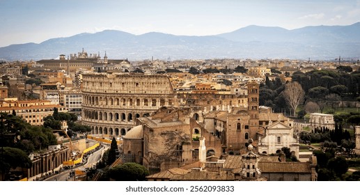 A panoramic view of Rome featuring the iconic Colosseum, surrounded by historical buildings and lush greenery, with mountains in the background under a clear sky.