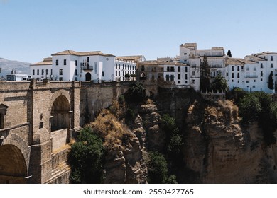 Panoramic view of Ronda, Spain showcasing the iconic Puente Nuevo bridge and charming whitewashed buildings perched on dramatic cliffs under a clear blue sky - Powered by Shutterstock