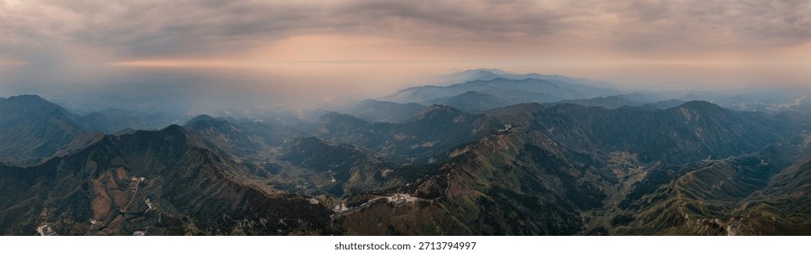Panoramic view of rugged mountain range with misty valleys under cloudy sky at sunrise