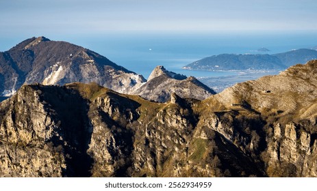 A panoramic view of rugged mountains with a distant coastline and ocean in the background. The landscape features rocky peaks and lush greenery, showcasing natural beauty. - Powered by Shutterstock