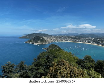 Panoramic view of a scenic coastal city, sparkling blue waters, and lush hills under a bright sky. - Powered by Shutterstock