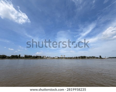 Panoramic view of the Scheldt river with distant city skyline under a wide blue sky with wispy clouds in Antwerpen, België