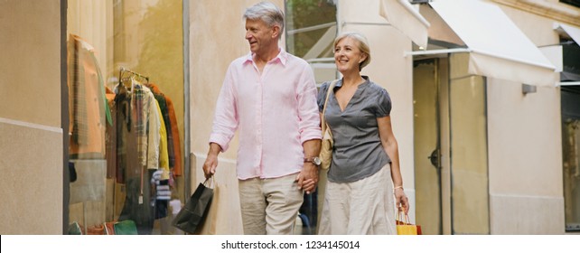 Panoramic View Of Senior Couple Walking In Luxury Shopping Street Carrying Bags, Vacation Trip, Outdoors. Healthy Mature Consumer People On City Break Travel, Leisure Recreation Lifestyle.