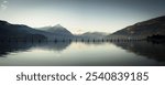 Panoramic view of a serene lake with snow-capped mountains in the background under a clear sky.