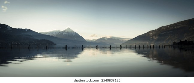 Panoramic view of a serene lake with snow-capped mountains in the background under a clear sky. - Powered by Shutterstock