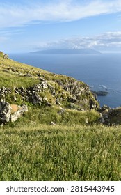 A panoramic view showing rugged cliffs overlooking the deep blue sea and remote Flores Island, Azores